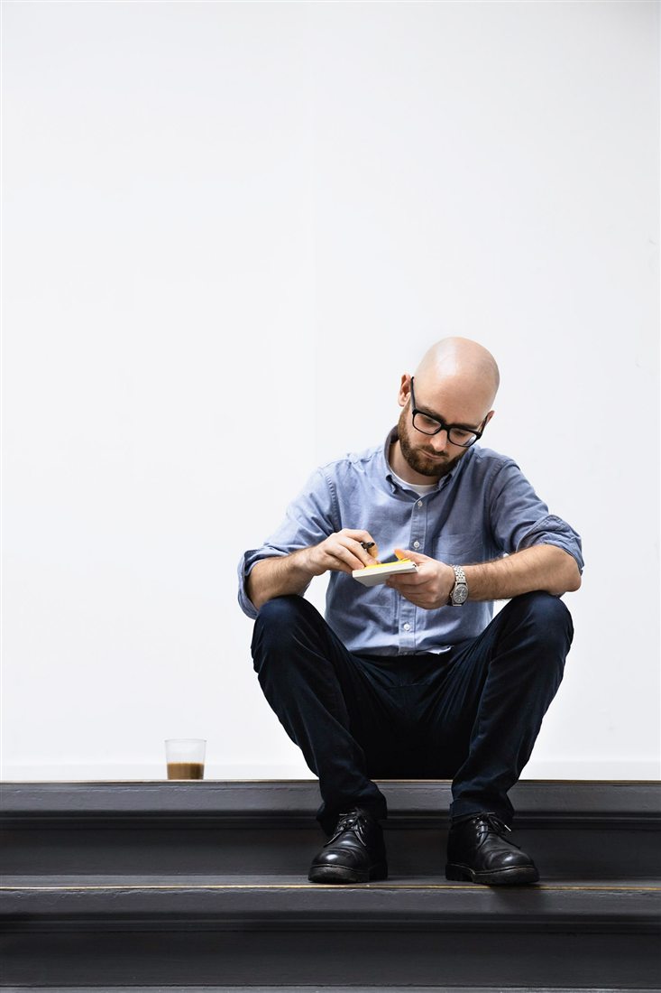 Sebastian sitting on a step, jotting in a notebook with a coffee glass beside him