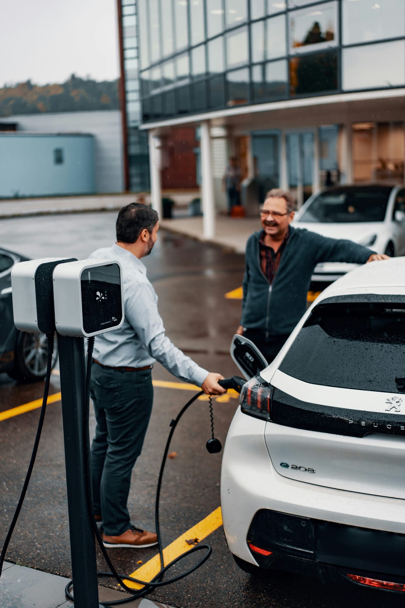 Two people in conversation next to an electric car at a charging station