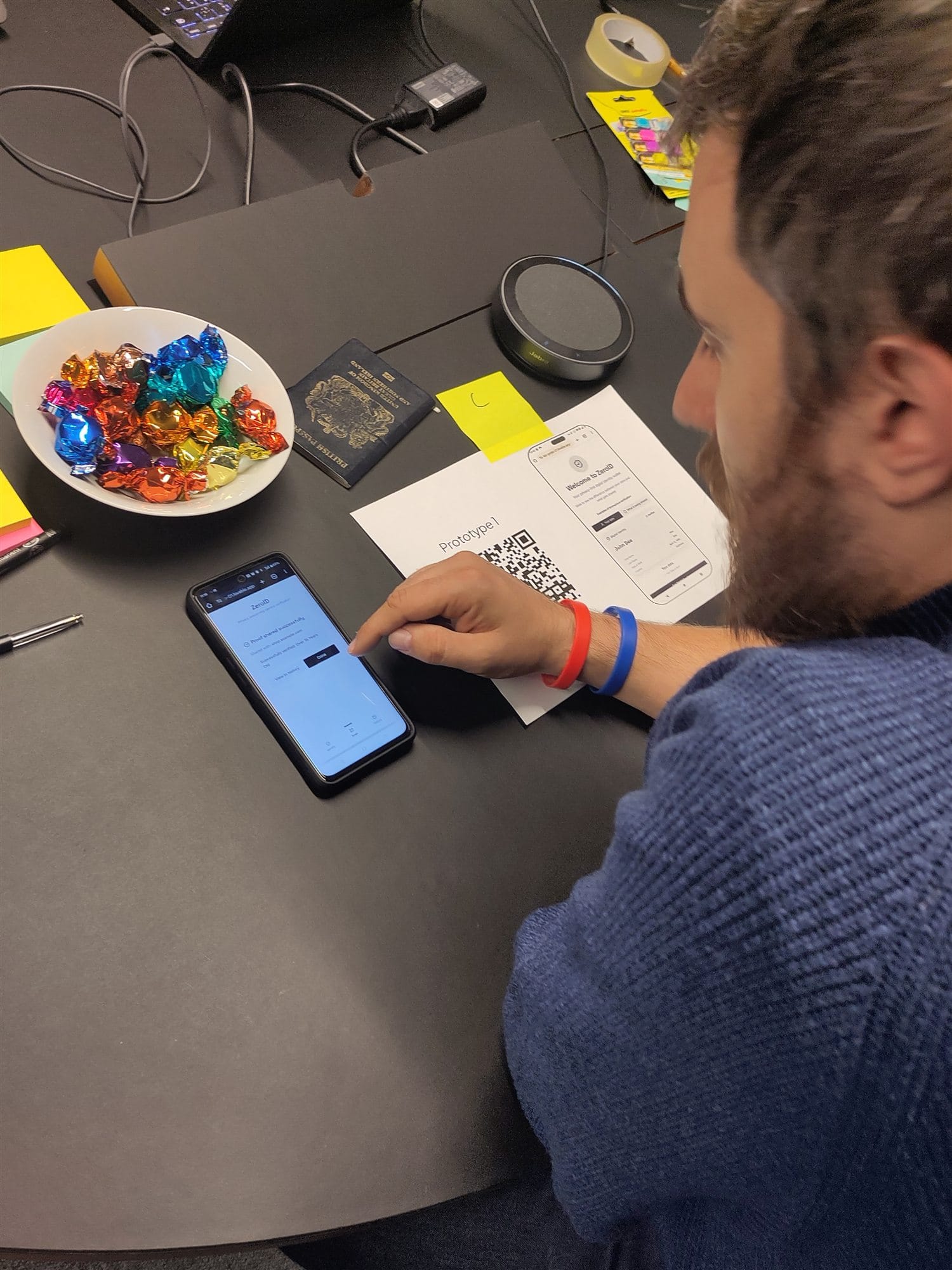 A participant in a London research session testing the prototype on a phone, with a printed prototype sheet, a QR code and a UK passport on the table
