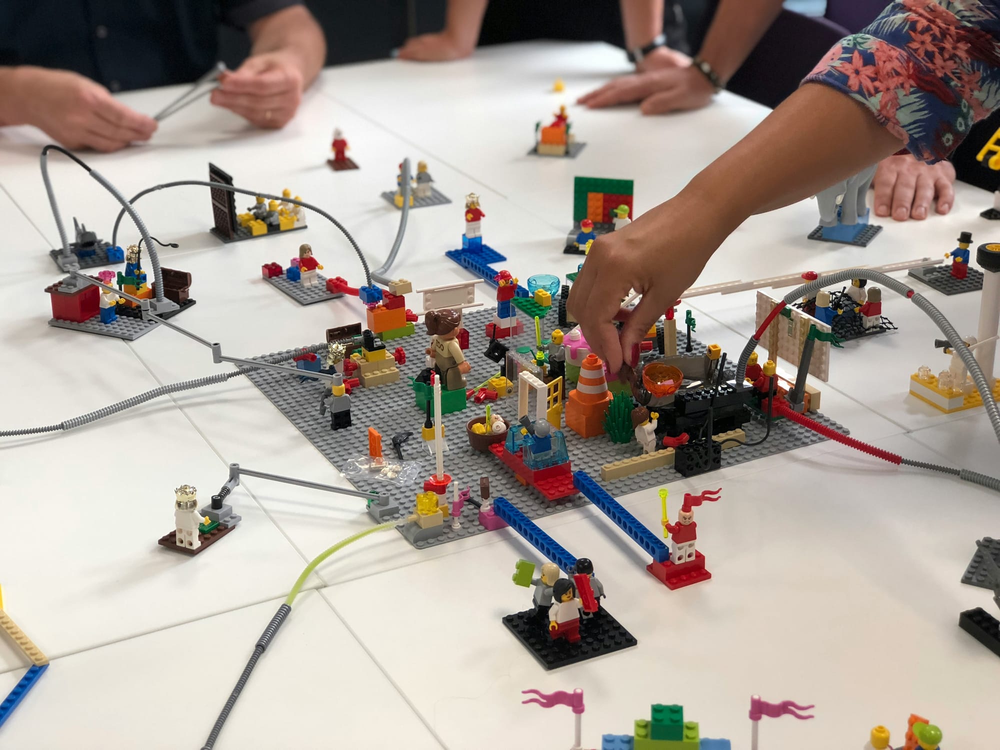 Hands arranging LEGO minifigures and builds across a table to map a journey