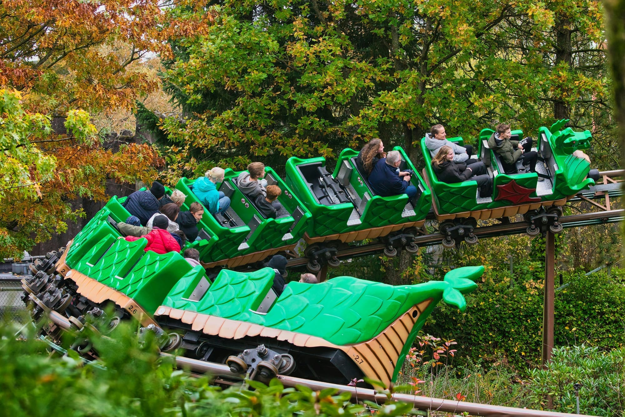 Families riding a green dragon rollercoaster through the trees at LEGOLAND