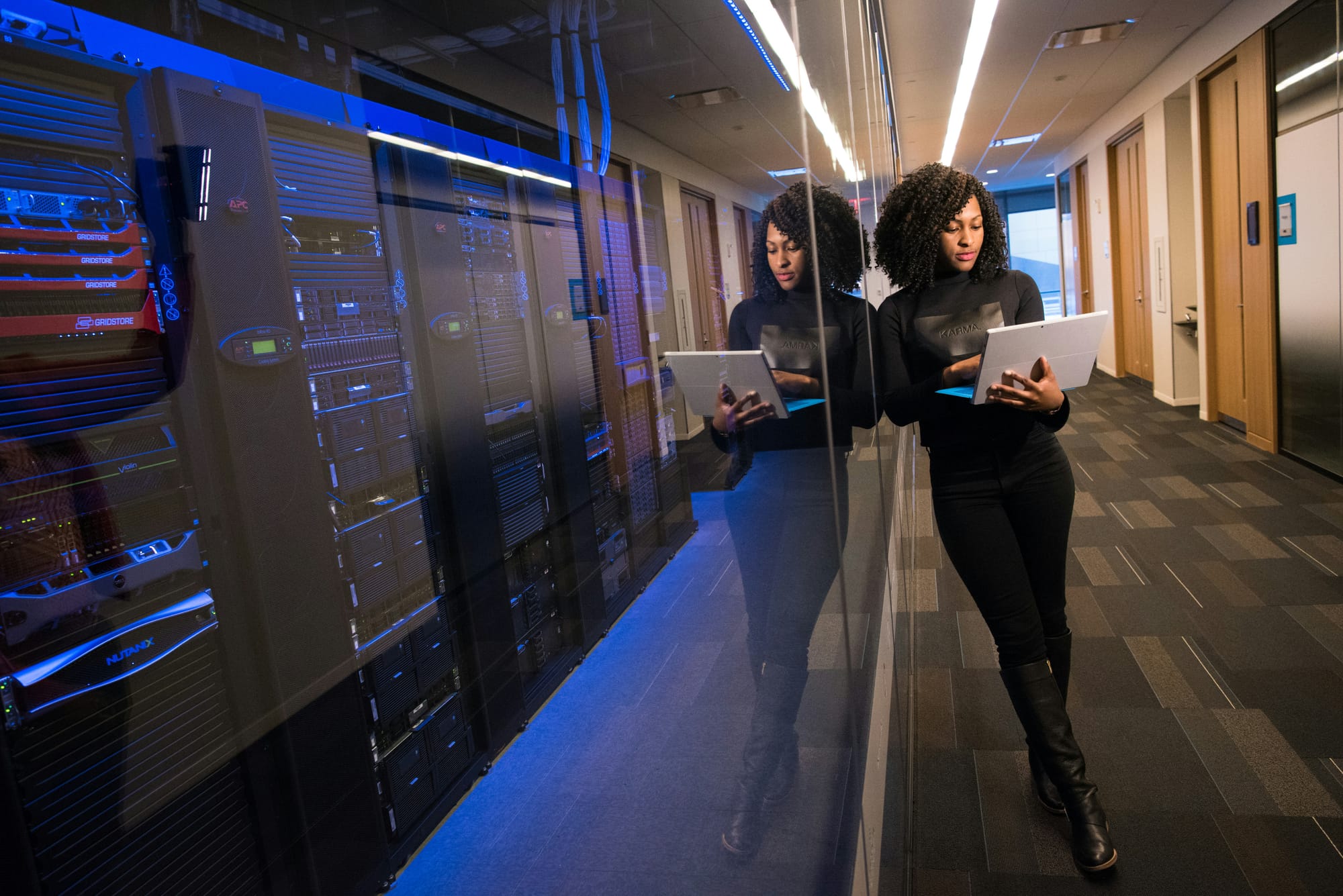 A person with a tablet beside server racks in a corridor