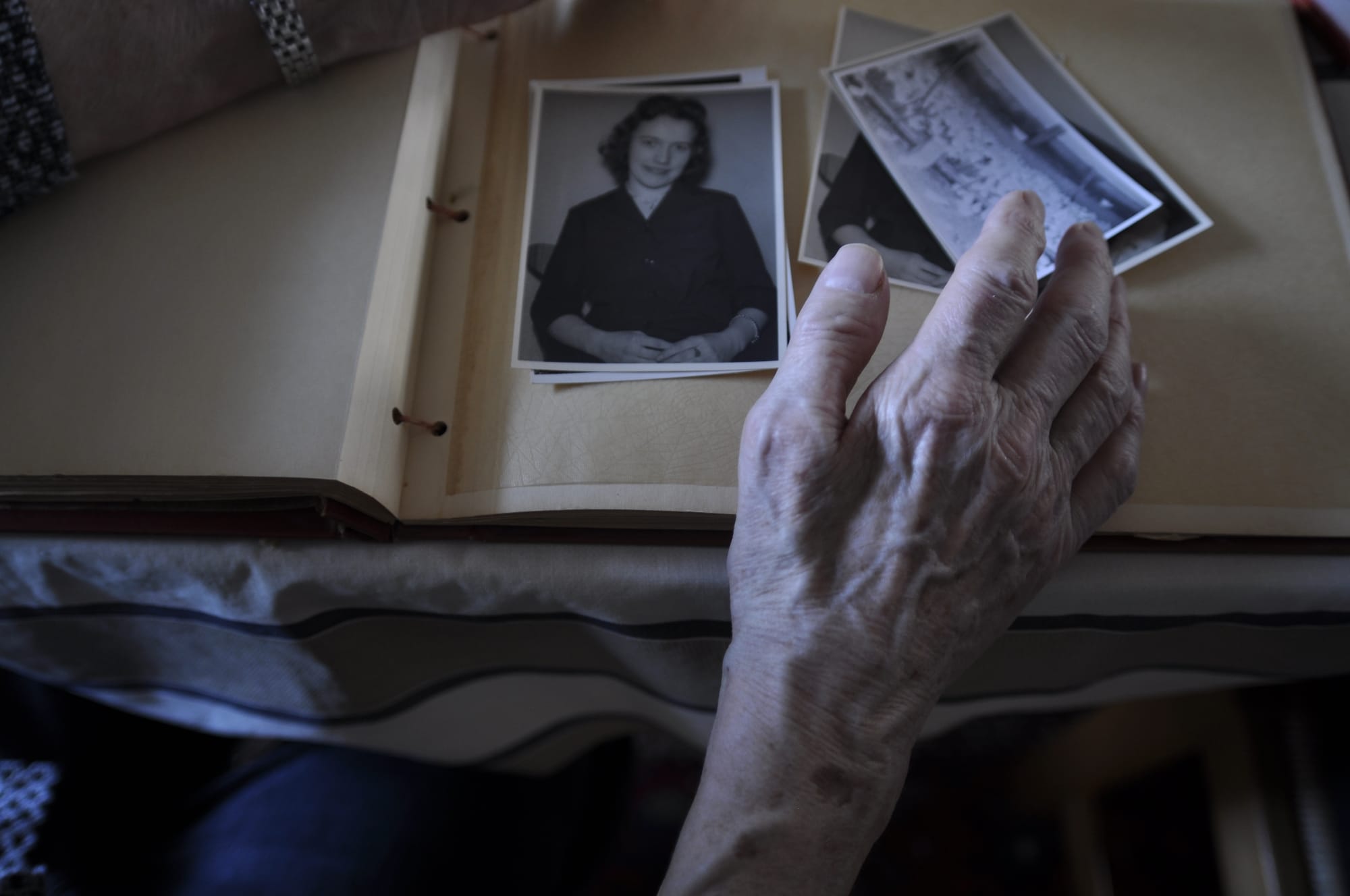 An elderly woman's hand resting on a photo album, over black-and-white photographs from her youth