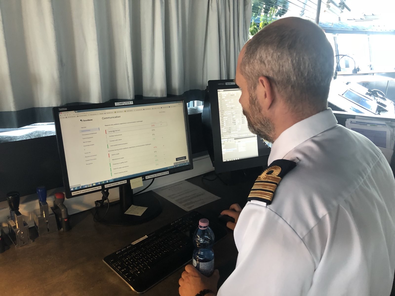 A ship's captain on the bridge, reviewing Scoutbase communication data on his monitor