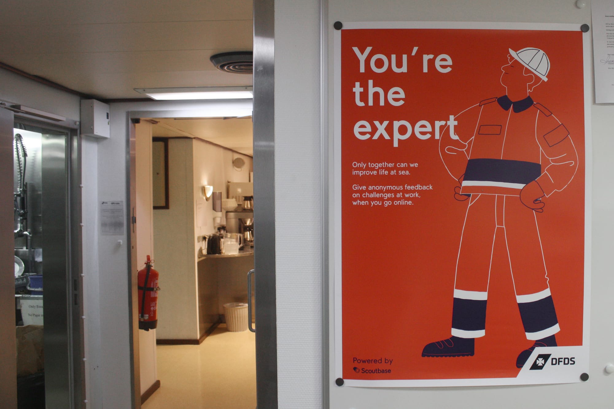 A 'You're the expert' Scoutbase onboarding poster on the wall of a DFDS vessel