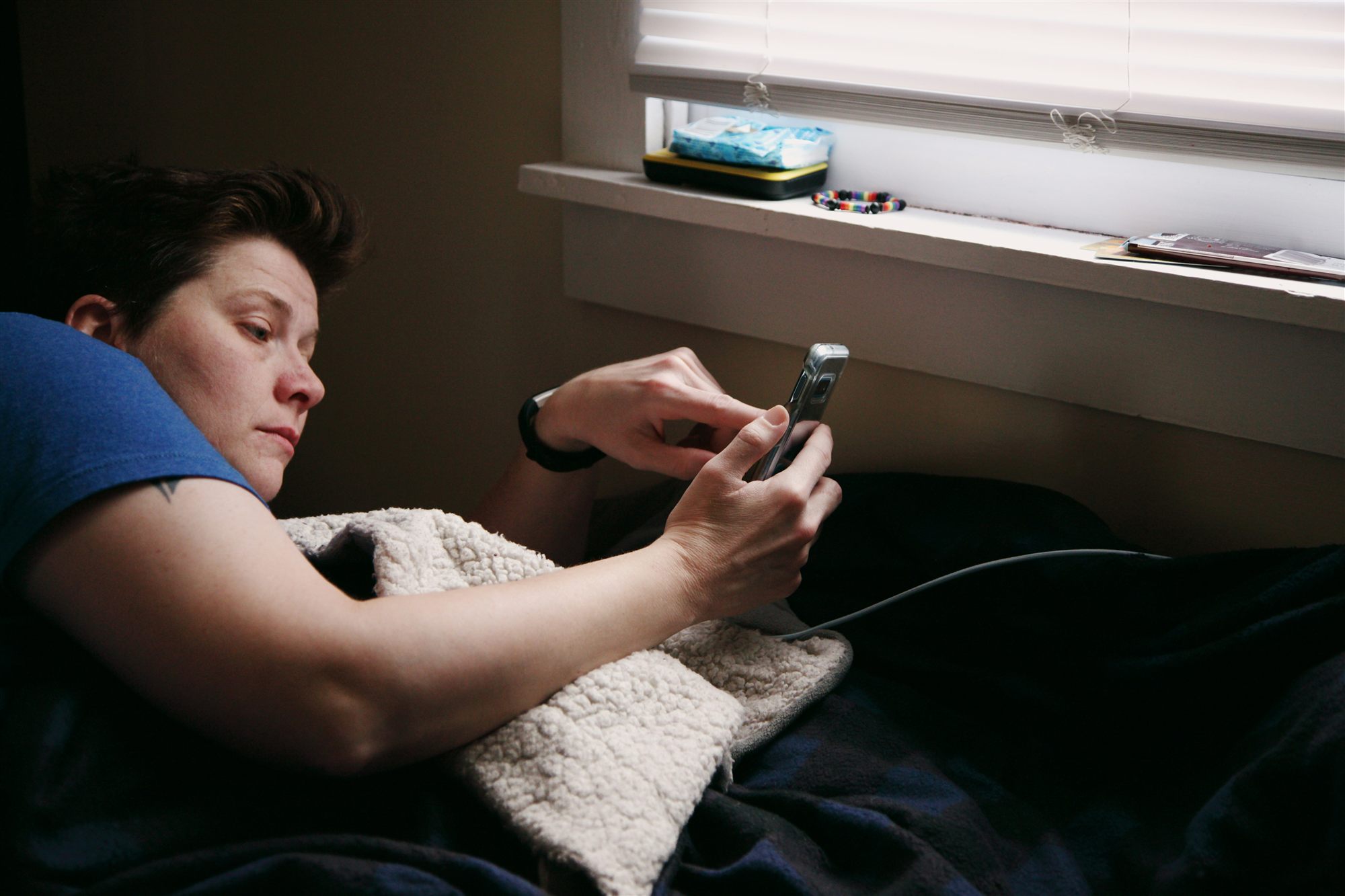 A person relaxing at home, checking their phone by a window